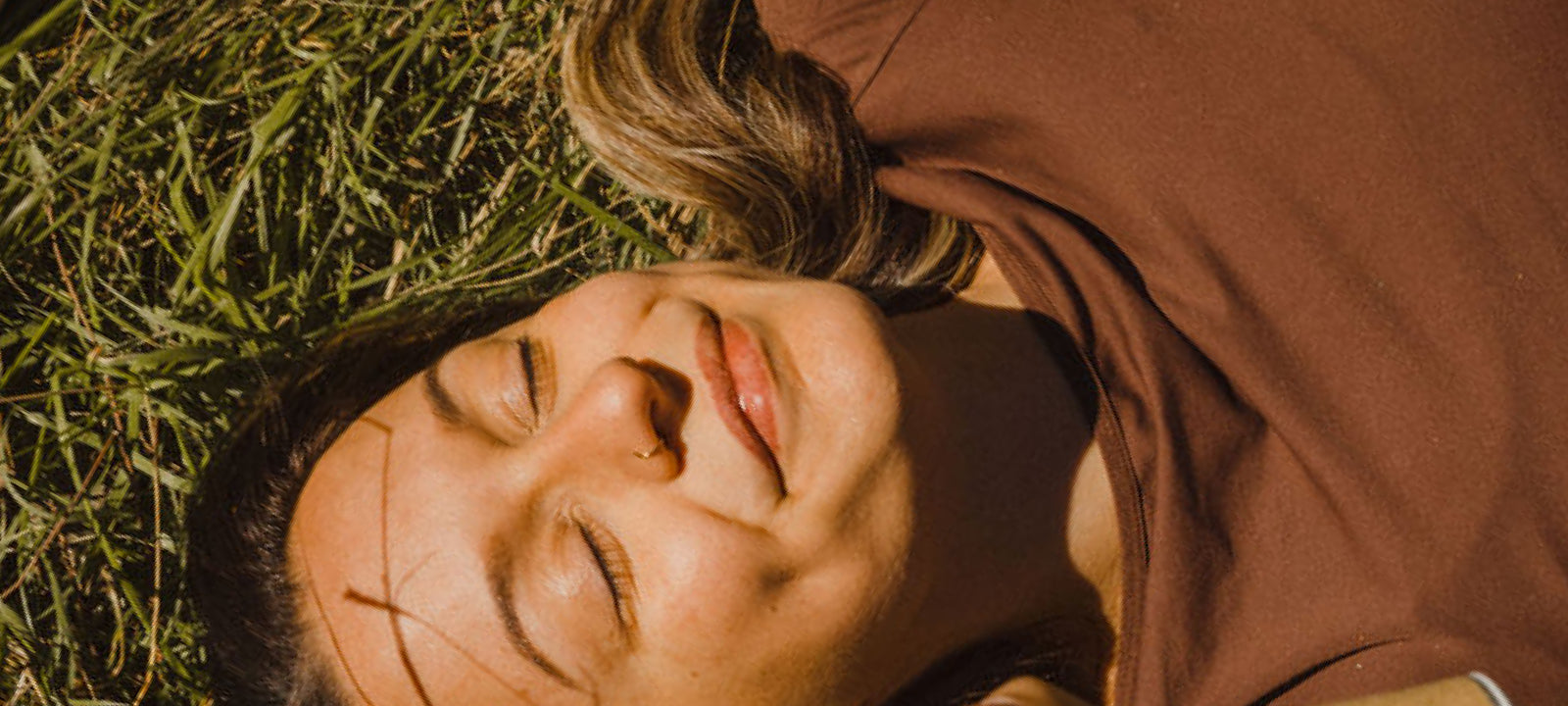 Woman in a brown top smiling with her eyes closed as the sun shines on her